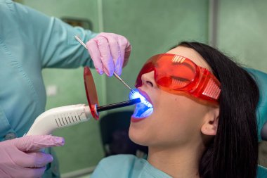 Diş hekimi hasta dişlerini ultraviyole lambayla inceliyor.