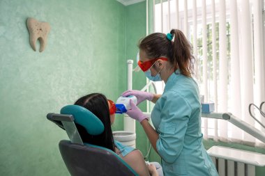 Kadın dişçi, dişçi hastasını ultraviyole lamba kullanarak dolduruyor. Diş beyazlatma prosedürü