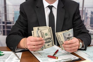 Genç ve şık bir iş adamı büyük miktarda para sayıyor ve ofisinde 1040 vergi formu dolduruyor. Büyük iş konsepti ve bundan kazanç.