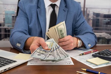 Tarz sahibi cesur bir adam 1040 vergi formatında çalışır ve dolar sayar. Vergi formları ve Amerikan doları kavramı.