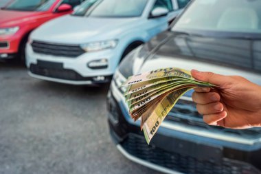 Otoparkta arabaların yanında büyük miktarda euro banknotları tutan genç ve güzel eller. İş konsepti. Araba konsepti
