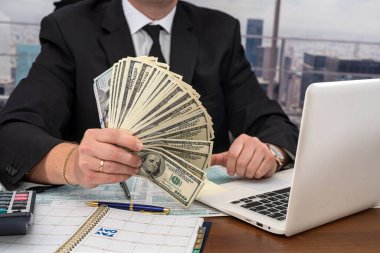 Genç ve şık bir iş adamı büyük miktarda para sayıyor ve ofisinde 1040 vergi formu dolduruyor. Büyük iş konsepti ve bundan kazanç.