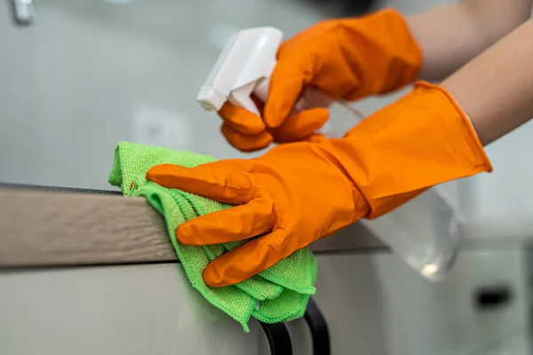 female housekeeping hands in gloves cleaning counter top in kitchen, close up. cleaning concept