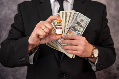 Takım elbiseli, güçlü elleri olan şık bir adam aşıyı kavanozda ve dolarla taşıyor. Aşı olmaya gelen bir adamın konsepti.
