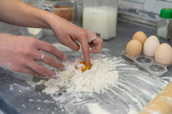 Beautiful young female hands break eggs into flour to knead a beautiful dough. Cooking concept