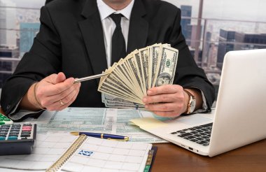 Geniş bir masada siyah şık takım elbiseli yakışıklı bir genç adam dolar sayıp form dolduruyor. Vergi formları ve dolar kavramı