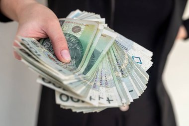 Genç kadın mutlu bir şekilde gülümsüyor, şehirde Polonya zloti paraları tutuyor. Cilalı banknotları olan başarılı kadın kavramı