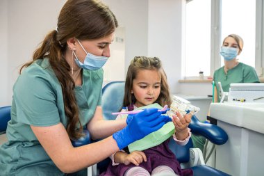 young specialist dentist woman brushes teeth and mouth at little client to prevent caries. The concept of brushing teeth in children