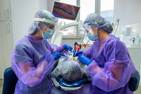 a patient with an ingrown tooth problem lies on an operating chair where he is operated on by a dentist and his assistants. The concept of surgery at the dentist