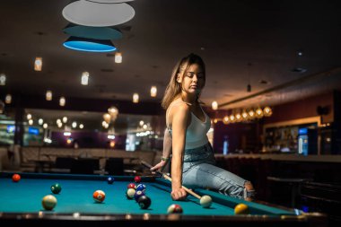 Elinde ıstakayla bilardo masasında oturan çekici esmer kadın. Oyundan sonra rahatla 
