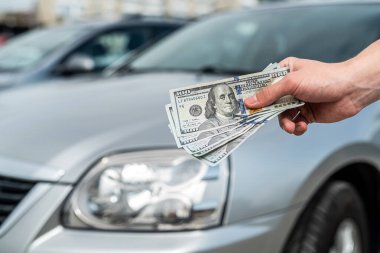 Man buys a modern car, holding dollar against auto in back. sale concept