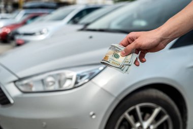 Man buys a modern car, holding dollar against auto in back. sale concept
