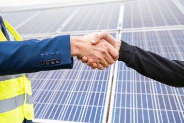 Tulum ve kask giyen işçiler panellerin montajı üzerinde çalıştıktan sonra iki adam el sıkışıyor. Çevreyi korumak için yeşil elektrik kavramı