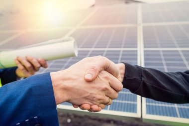 Tulum ve kask giyen işçiler panellerin montajı üzerinde çalıştıktan sonra iki adam el sıkışıyor. Çevreyi korumak için yeşil elektrik kavramı
