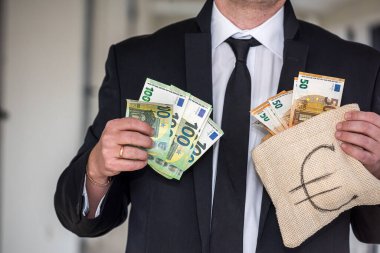 Kravatlı, pahalı takım elbiseli genç patron iş adamı çantasında avro banknotları tutuyor. Erkekler için Euro çanta konsepti
