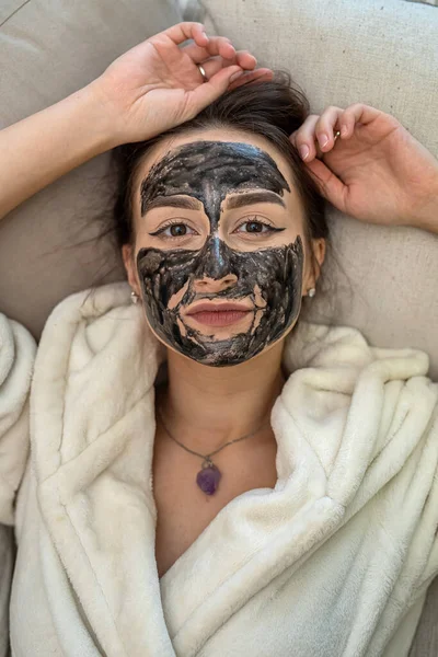 young woman makes herself a black clay regenerating mask that smoothes wrinkles. The concept of a rejuvenating mask for a woman