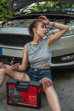 Genç kadın tamir için aletleri tutuyor ve bozuk arabanın yanında yardım bekliyor. yaz zamanı