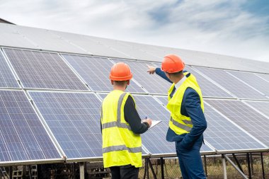 Üniformalı ve miğferli ustabaşı işadamına güneş panelleri kurma planını anlatıyor. Yeşil elektrik kavramı