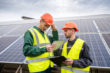 Güneş panellerini inceledikten sonra özel kasklı iki genç adam not alıyor. Yeşil enerji tasarrufu kavramı