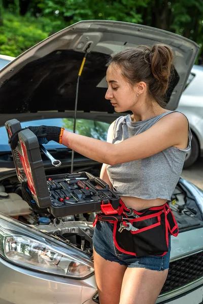 woman holding work tools standing near broken car and waiting for help. female driver is confused and doesnt know what to do