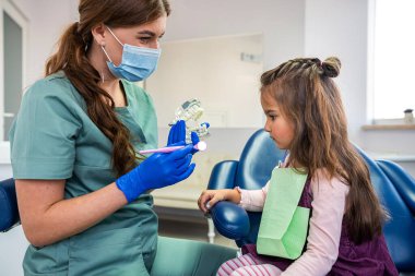 Diş hekimi, çocuk hastaya klinikteki minyatür çenelerde diş fırçasını nasıl kullanacağını gösteriyor. Sağlık Hizmetleri  