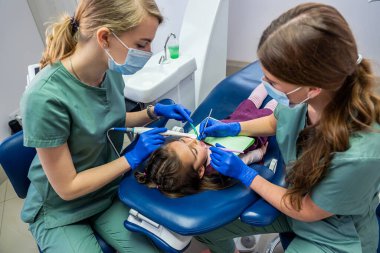 Nitelikli dişçiler çocukların dişlerini yeni profesyonel ekipmanlarla kontrol ediyorlar. Çocukların dişlerini kamerayla incelemek.