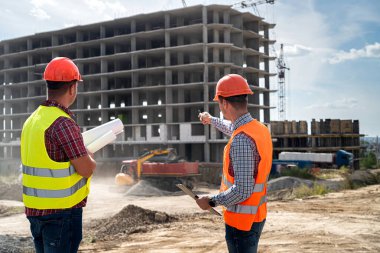 Özel giyimli ve üniformalı iki genç işçi inşaat alanında bir ev inşa etme sürecini tartışıyor. İnşaat konsepti