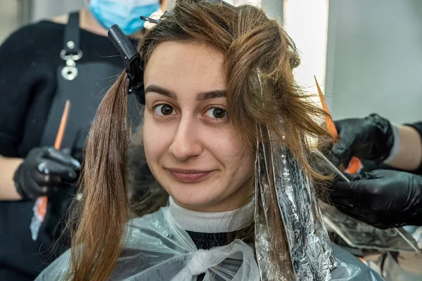 a girl with dark hair came to the salon to lighten it and paint it a different color. Hair coloring concept during a pandemic