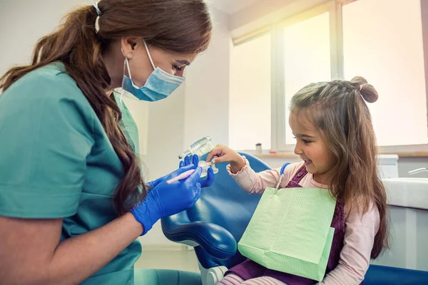 Dişçi randevusunda küçük bir çocuk, doktor yapay çenelerde dişlerini nasıl fırçalayacağını gösterir ve söyler.