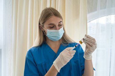 Eldivenli ve maskeli genç çekici hemşire aşı için şırınga ile aşı çiziyor. İnsanları koronavirüse karşı aşılama kavramı