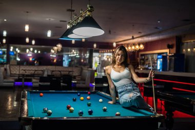 Güzel genç bayan bilardo masasında oturuyor, maçtan sonra rahatla. Bilardo