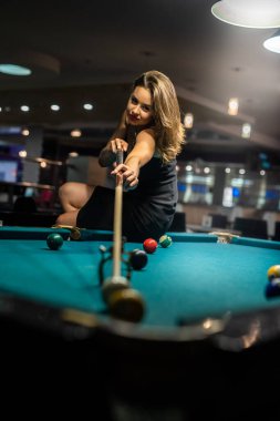 Güzel bir kadın elinde ıstakayla bilardo masasının kenarına oturur. Yaşam biçimi