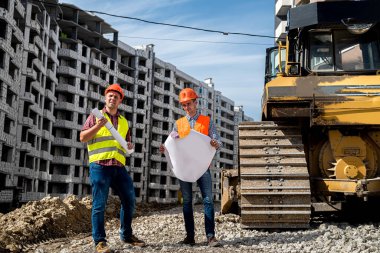 İşçiler işçi tulum ve kask giyip yeni binanın yanında duran bir planla güçlüler. İnşaat konsepti