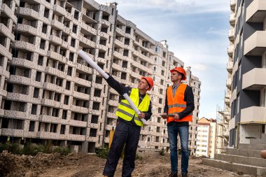 Yakışıklı, güçlü, özel elbiseli bir işçi eve el attığını ve diğerinin yakınlarda durduğunu gösteriyor. İnşaat konsepti