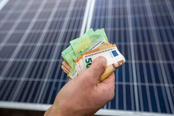 strong male hands of a worker holding euro banknotes for work done. The concept of payment for the installation of solar panels