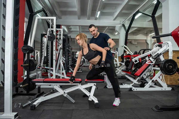 Fit female client working out with personal male instructor with heavy dumbbells at the gym. sport for healthy lifestyle