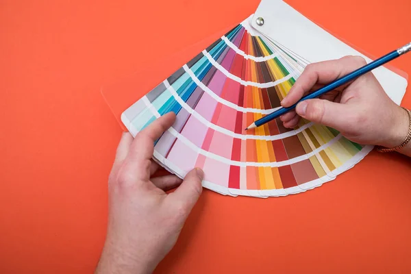 male hand choose color in palette samples. Rainbow colors catalogue isolated on orange background