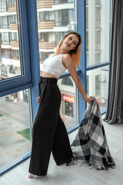 sexy flexible perfect girl in dark black pants and white top curves near a spacious window. Beauty girl concept by the window