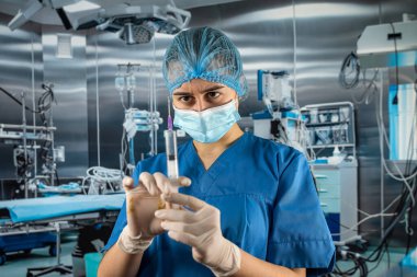 Mavi üniformalı genç bayan doktor elinde şırıngayla hastayı bekliyor.