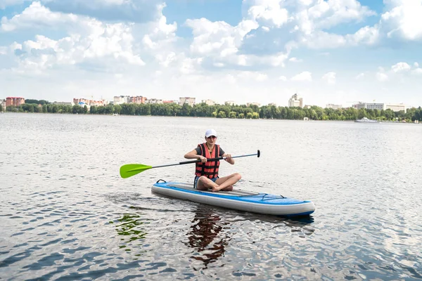beautiful young woman in a protective vest learns to swim on a sup board on a city lake, active lifestyle, summer time