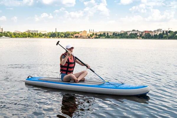 Young woman sitting on paddle board wear life vest and learn how swim, summer active lifestyle