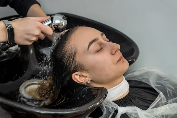 a brand new master colorist on his working day in a prestigious salon washes the mask from the client\'s hair. Concept of masters of colorists