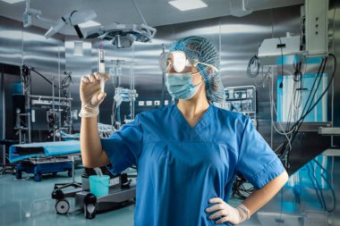 Kadın doktor ya da asistan ameliyat odasında şırınga ile ilaç bulundurmaktan korunmak için eldiven, yüz maskesi ve şapka takıyor. 