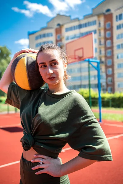 Young woman throws a basketball outdoors on a sunny day. Outdoor basketball concept