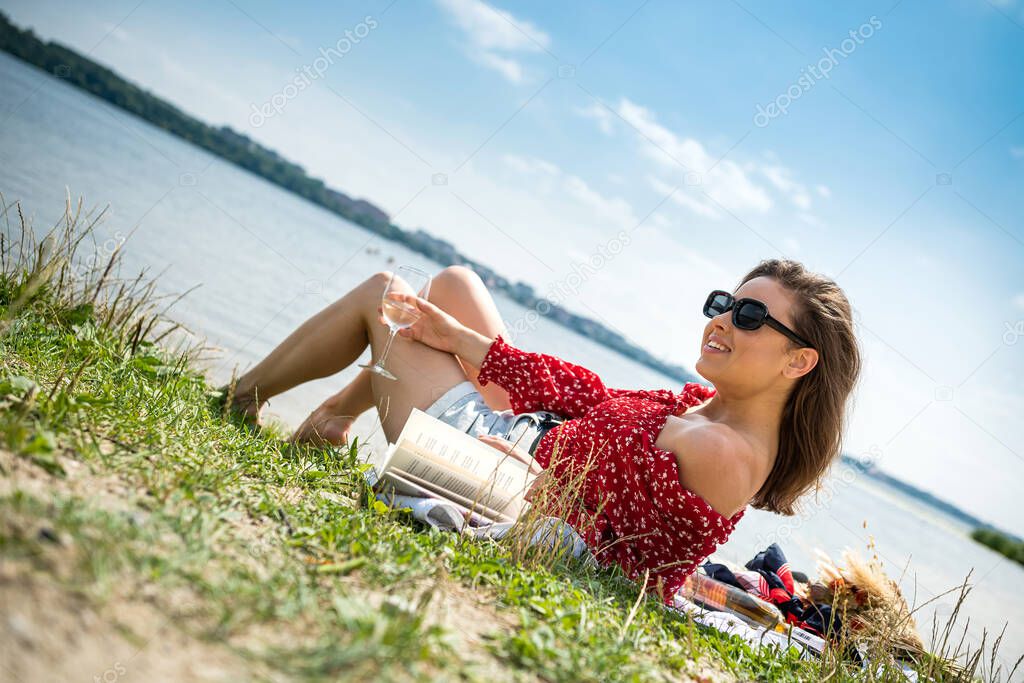 beautiful girl wear casual cloth hold glass of champagne or white wine alone rest near lake, summer day
