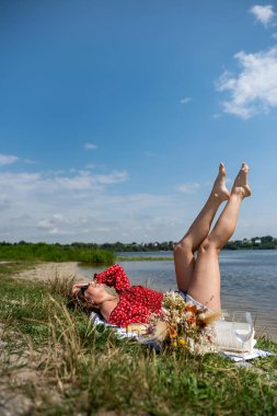 Genç kadın göletin kenarında oturuyor ve dinleniyor. Sıcak yaz gününün tadını çıkarıyor. Yaşam biçimi