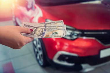 Güzel, sağlıklı bir adamın elinde bir araba galerisinde yeni pahalı arabaların yanında yuvarlak bir miktar banknot tutuyor. İş konsepti. Seçim konsepti