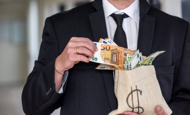 A middle-aged man in a business shirt holds a bag of dollars with an angry face. The concept of money you do not want to give
