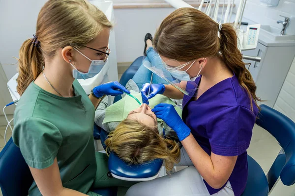 Maskeli dişçi ve asistan diş hekiminde kadın hastaları tedavi ediyor. stomatoloji