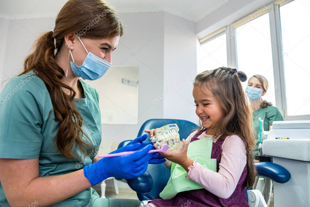 Dentist showing child patient how to use tooth brush on miniature jaws at clinic. Healthcare  